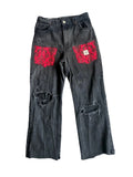 Black distressed jeans with red floral patches on a textured gray surface